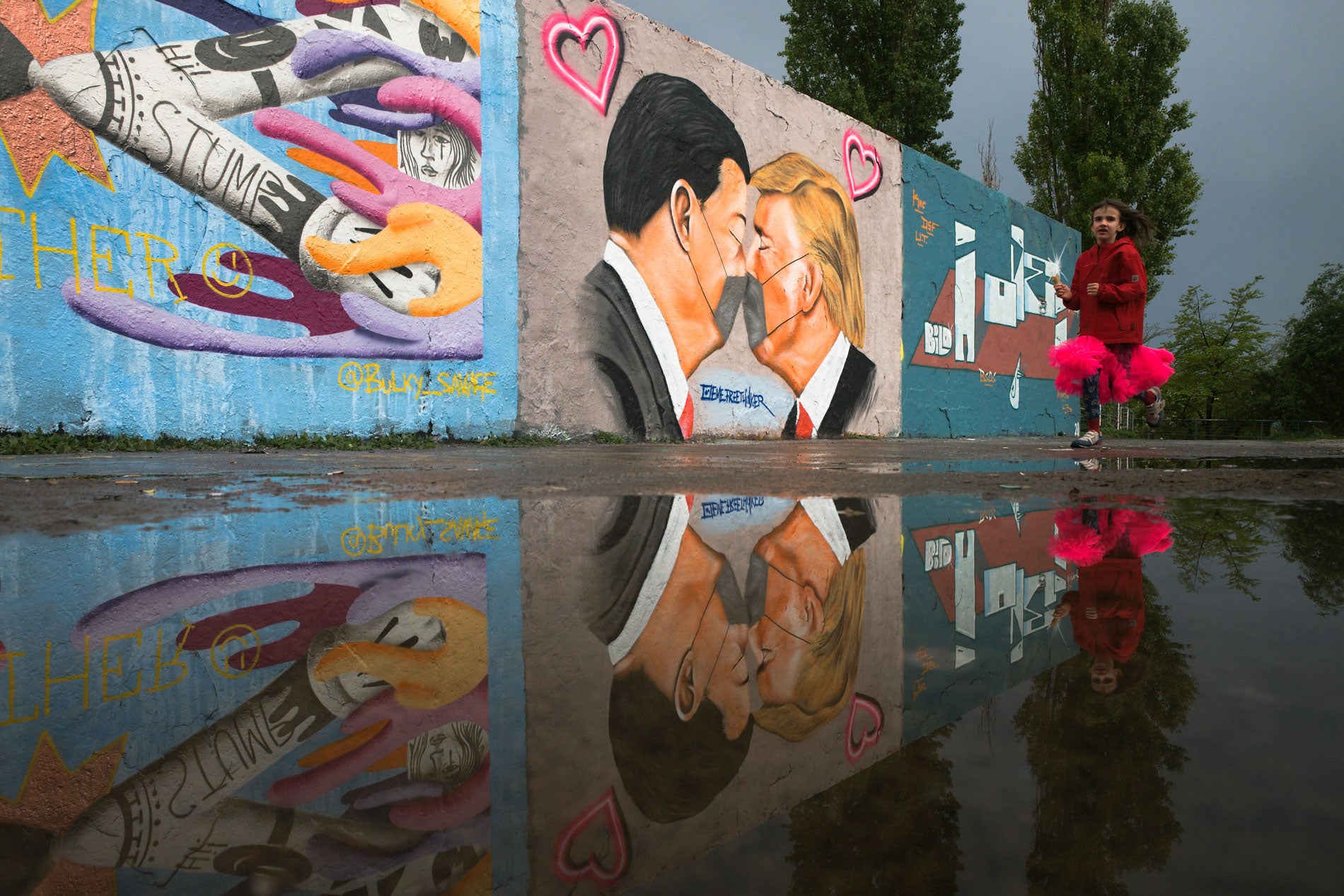A girl runs in front of graffiti depicting US President Trump and China's President Xi Jinping with face masks displayed on a wall in Berlin, Germany, April 29, 2020.
