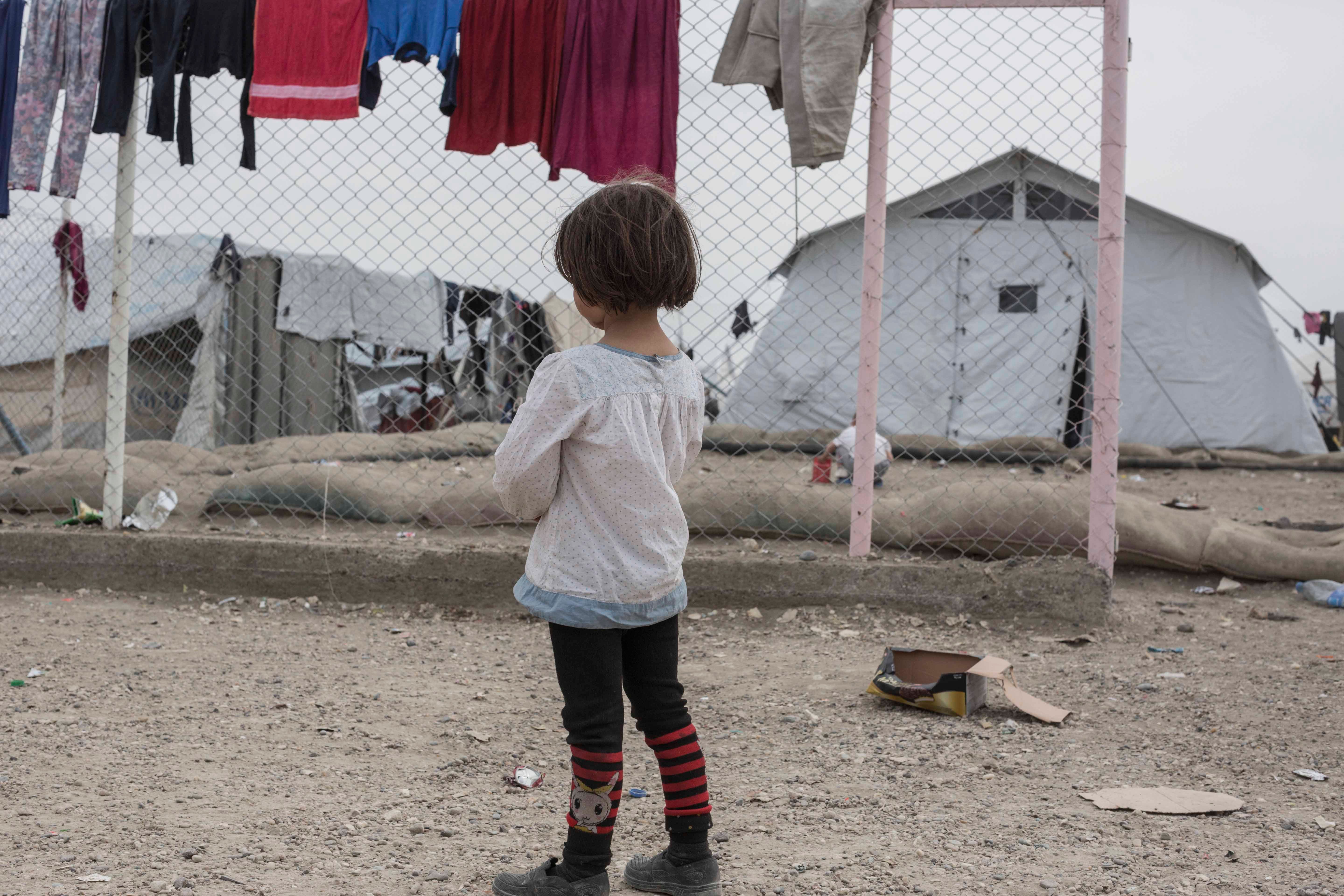 A girl stands in front of a chainlink fence