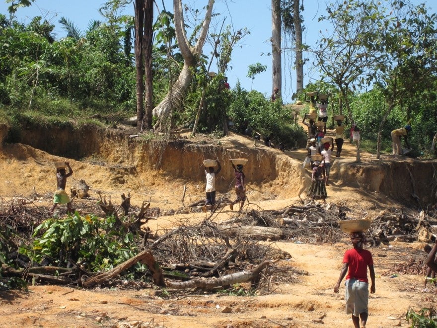 A wide shot of people carrying pans on their heads in a mining site