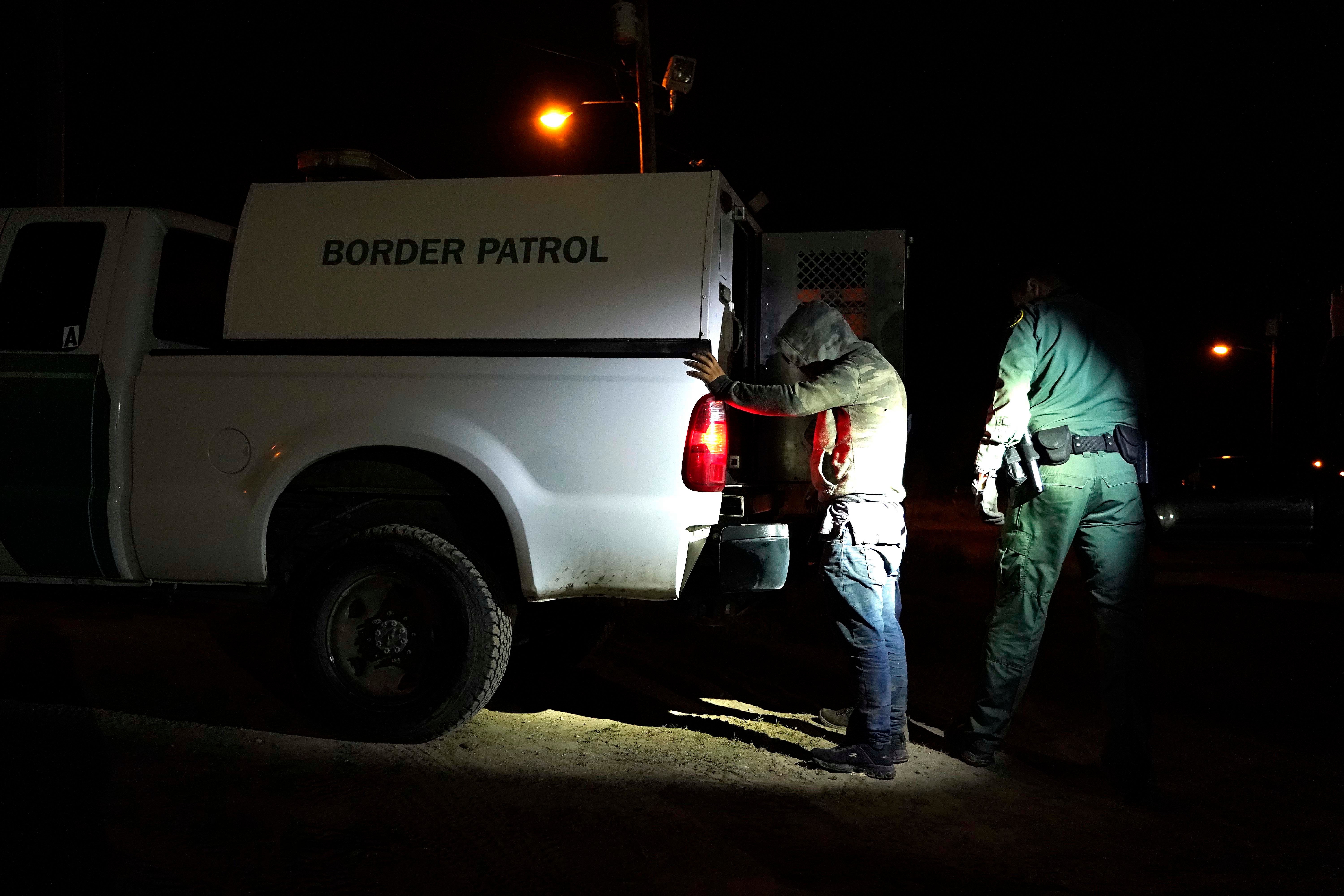 A man stands with his hands on the back of a van marked "Border Patrol"