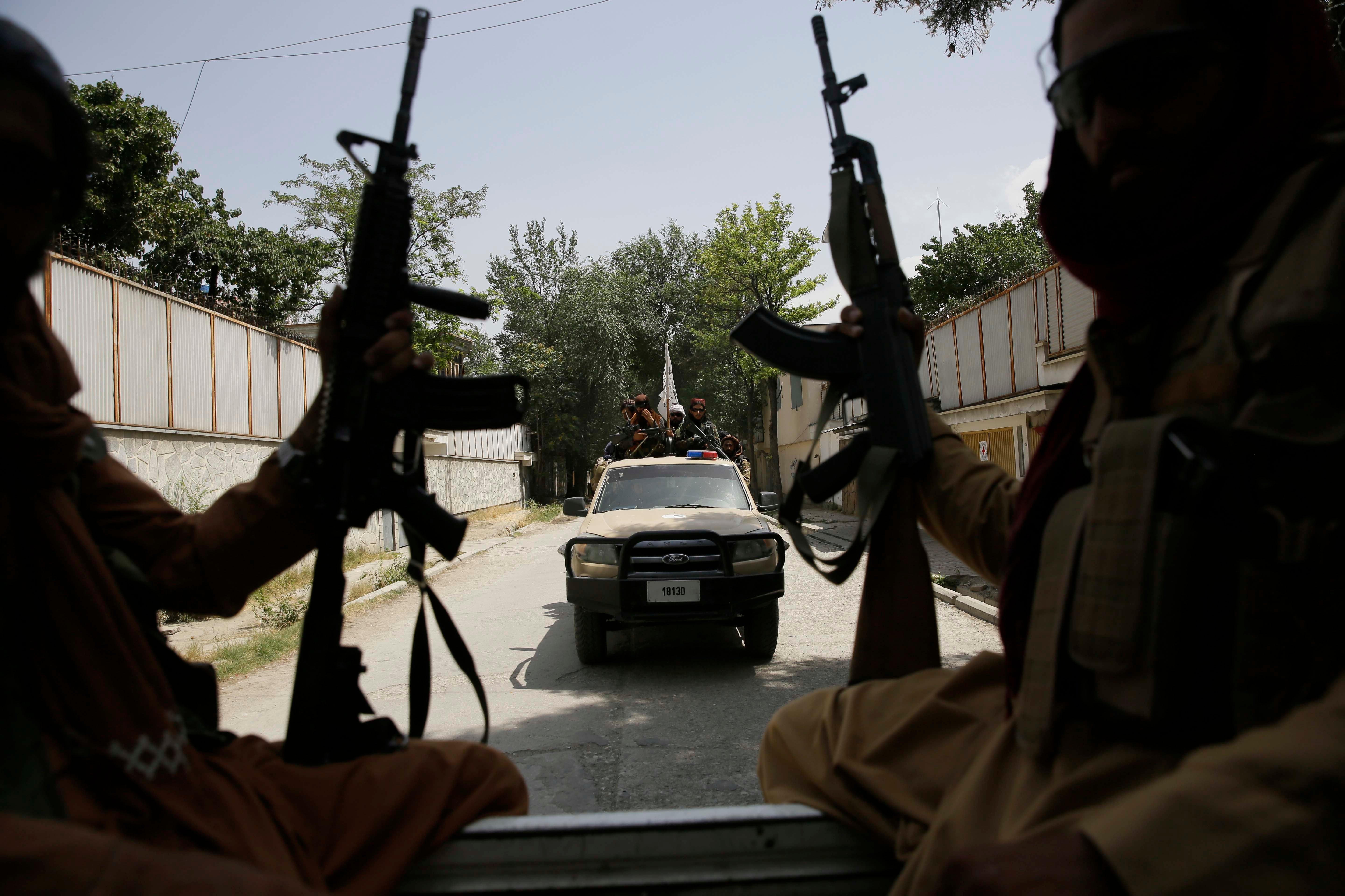 Two men holding weapons ride in the bed of a truck