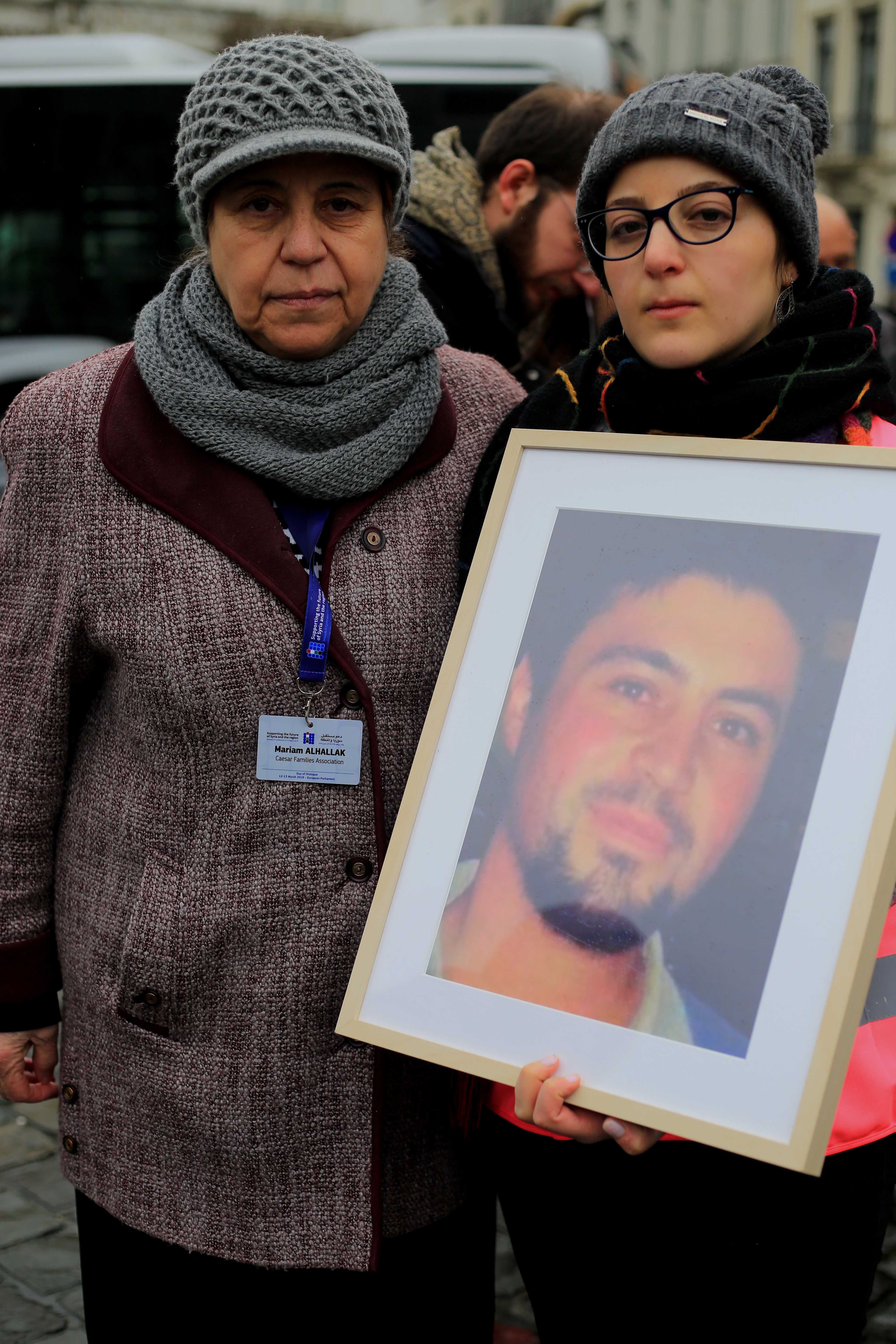 Two women hold a photo of a man 