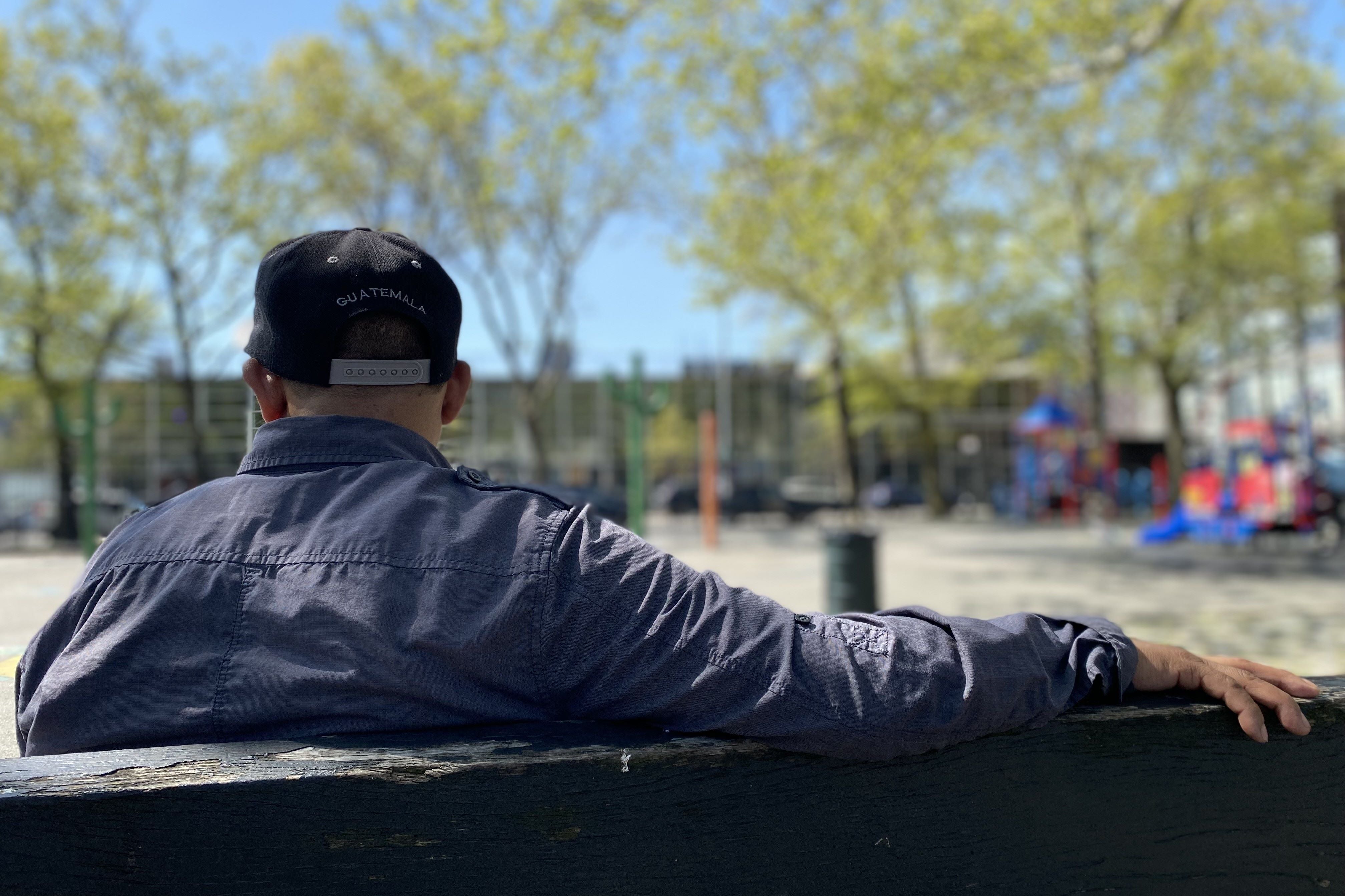A man wearing a "Guatemala" hat sits on a bench with his back to the camera