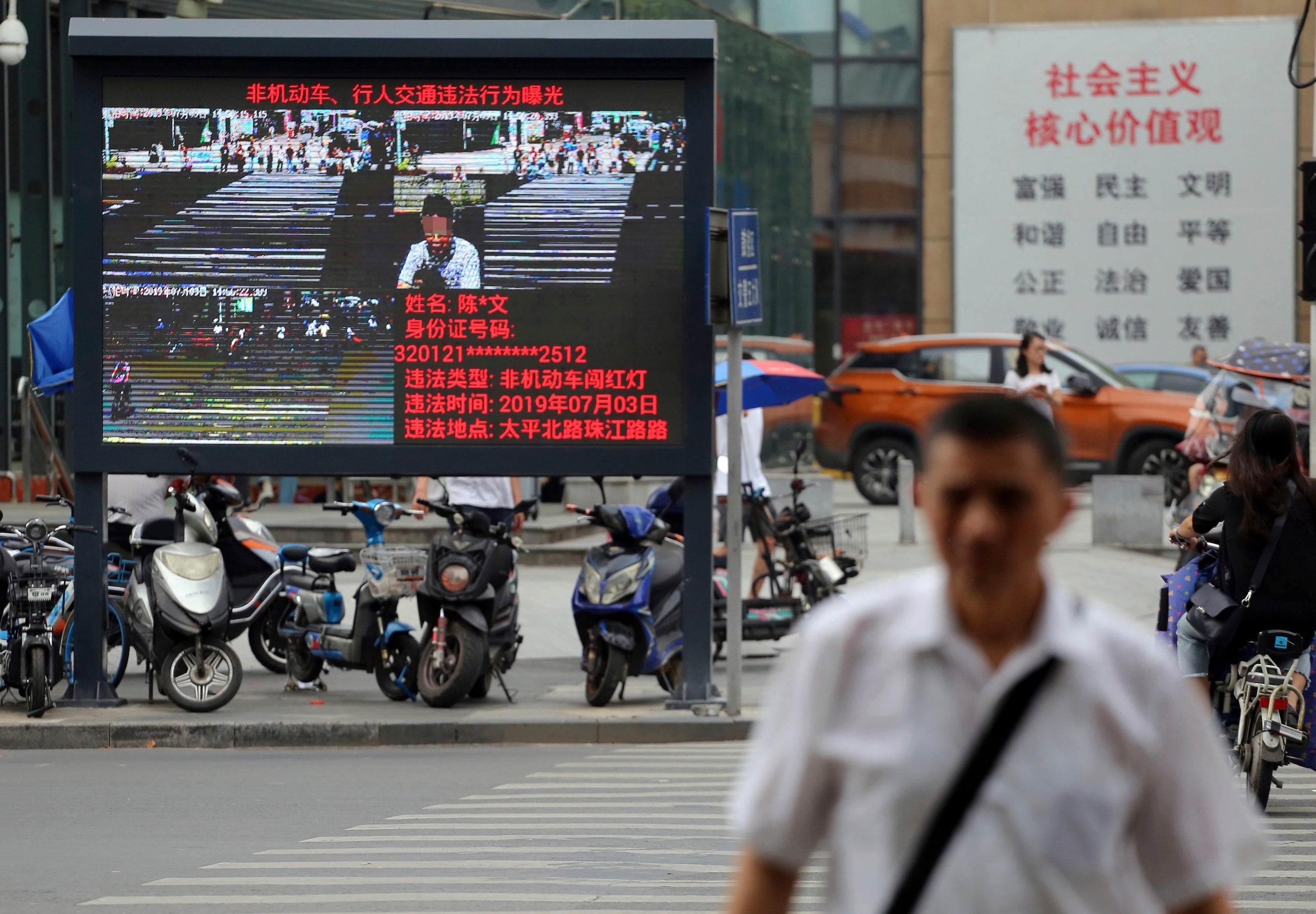 Pedestrians walk across a crossroad as a big electronic screen supported by face-recognition system shows the image of a jaywalker at the intersection in Nanjing city, east China's Jiangsu province, July 4, 2019. 