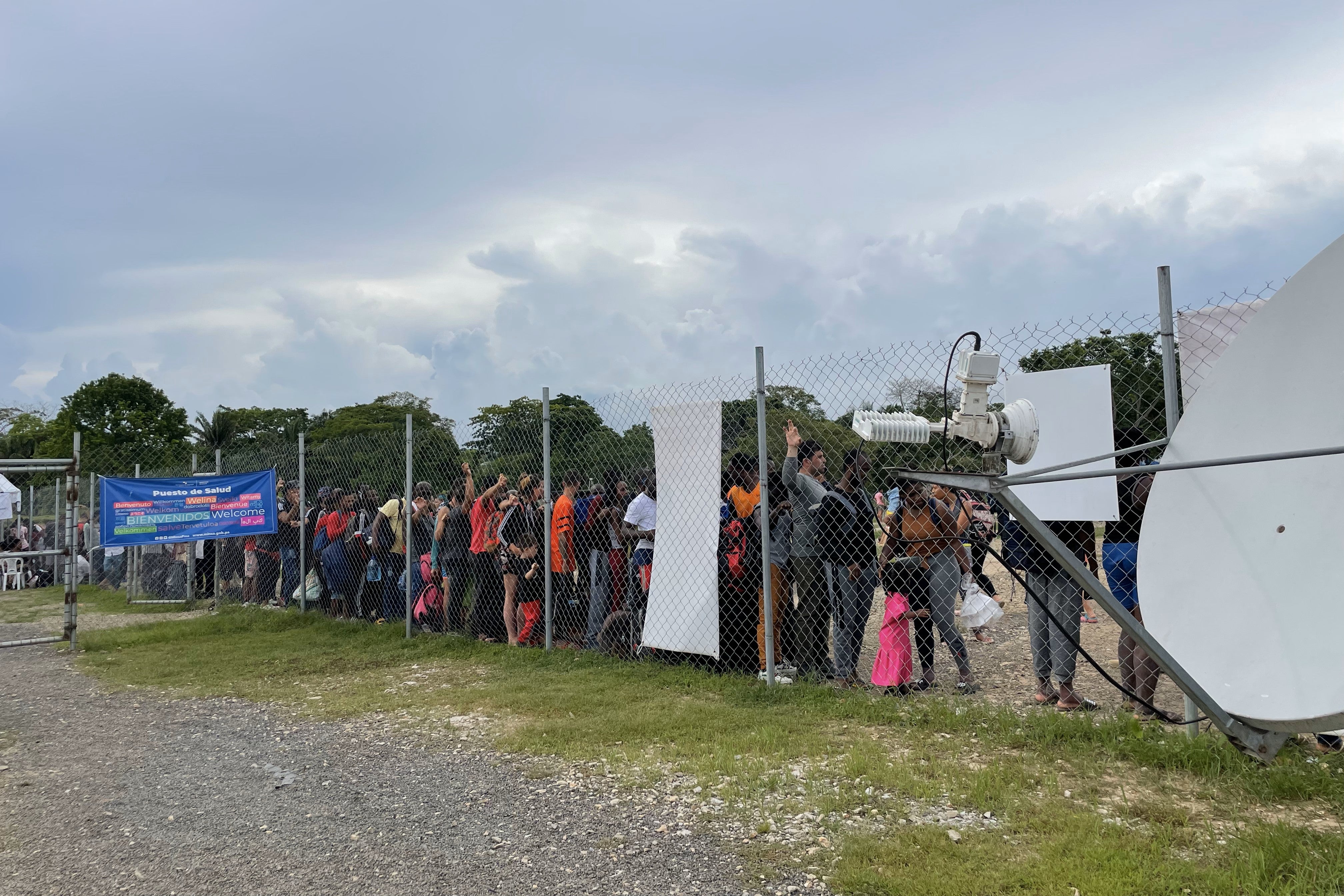 Migrants and asylum seekers wait behind a wire fence