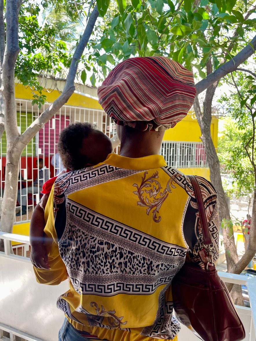 A young women is pictured holding a small infant with her back turned to the camera.