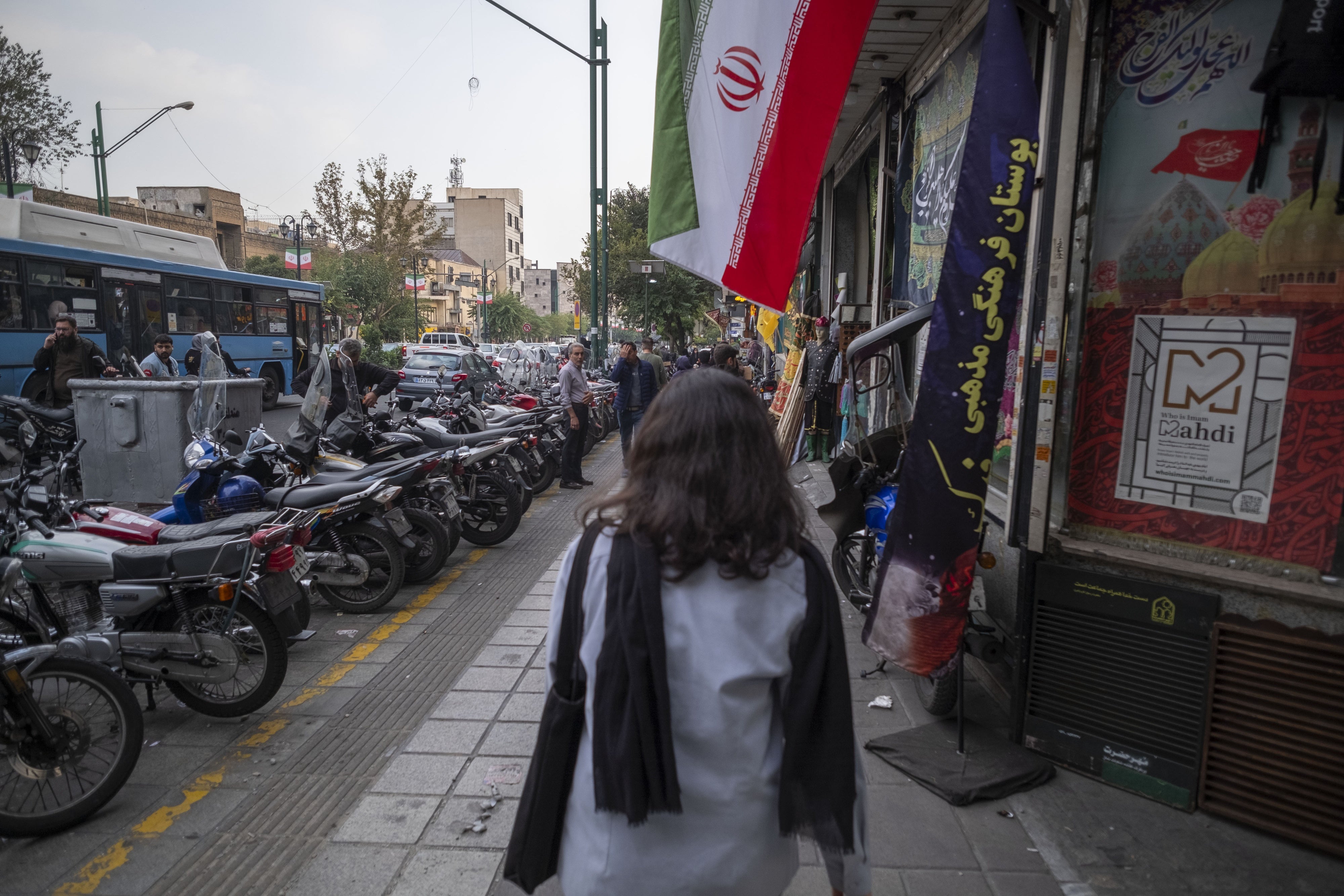 A young Iranian woman, who does not wear a mandatory headscarf, walks under an Iranian flag in downtown Tehran, Iran, September 29, 2024. 