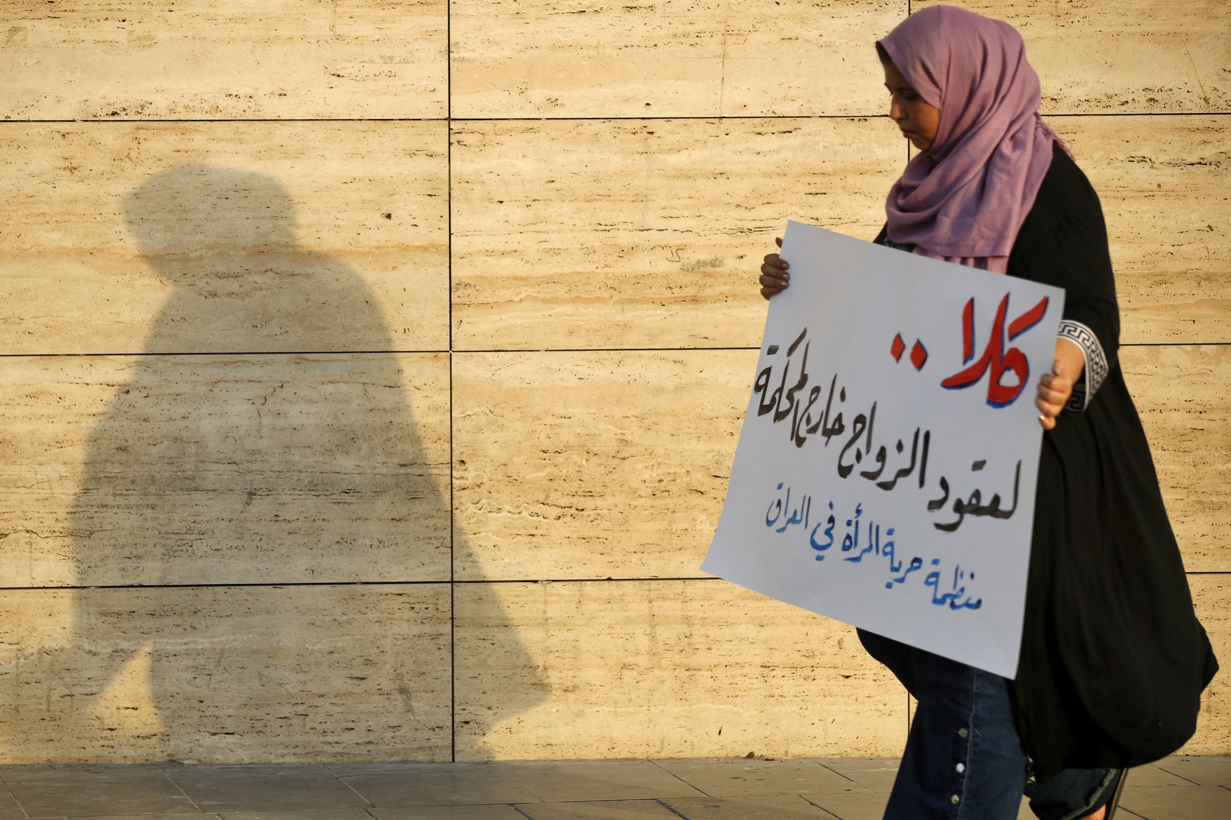 A woman walks holding a placard as activists demonstrate against female child marriages, in Tahrir Square, central Baghdad, July 28, 2024. 