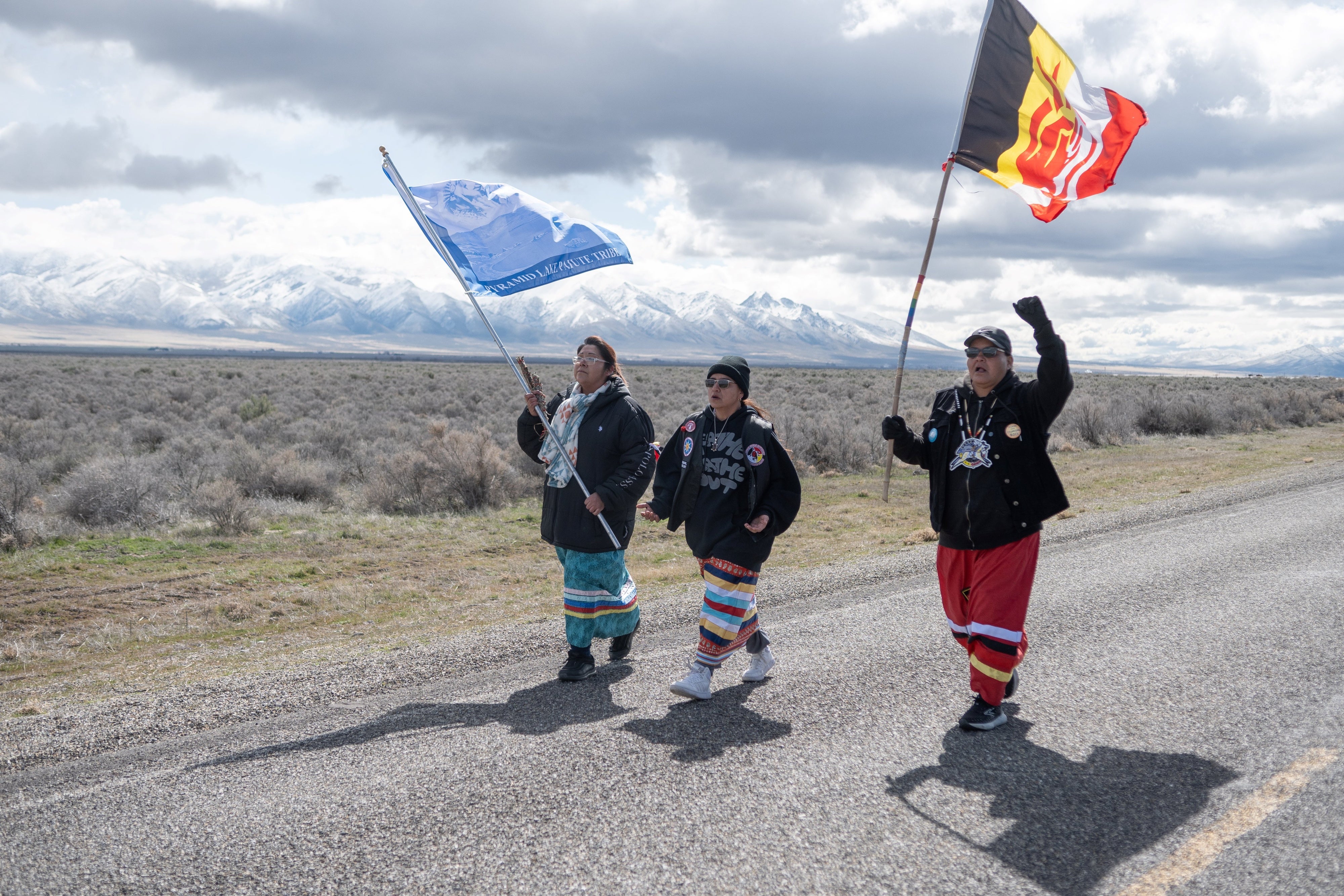 Three indigenous women carrying flags on a rural road