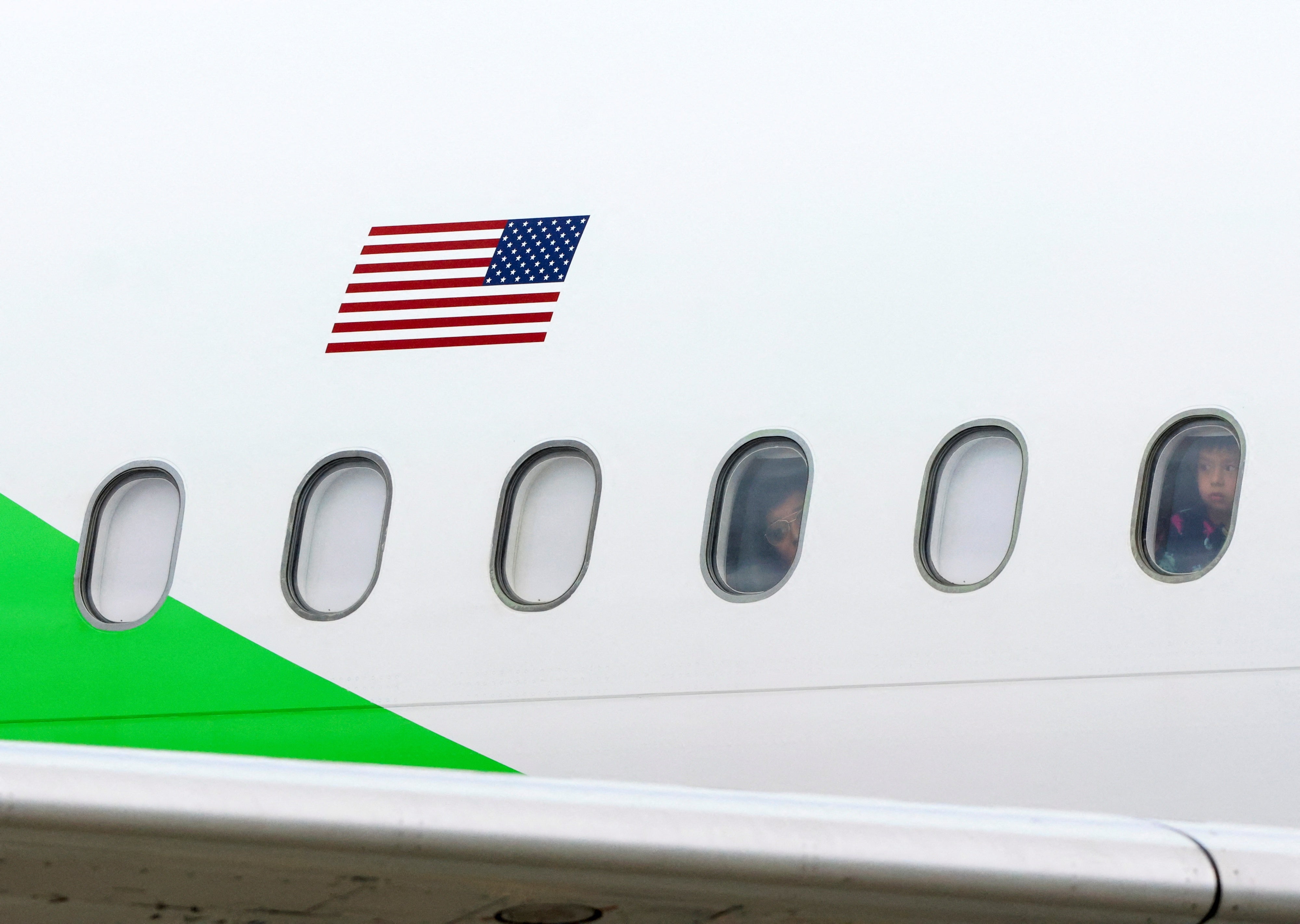 Migrants look out the windows of a plane