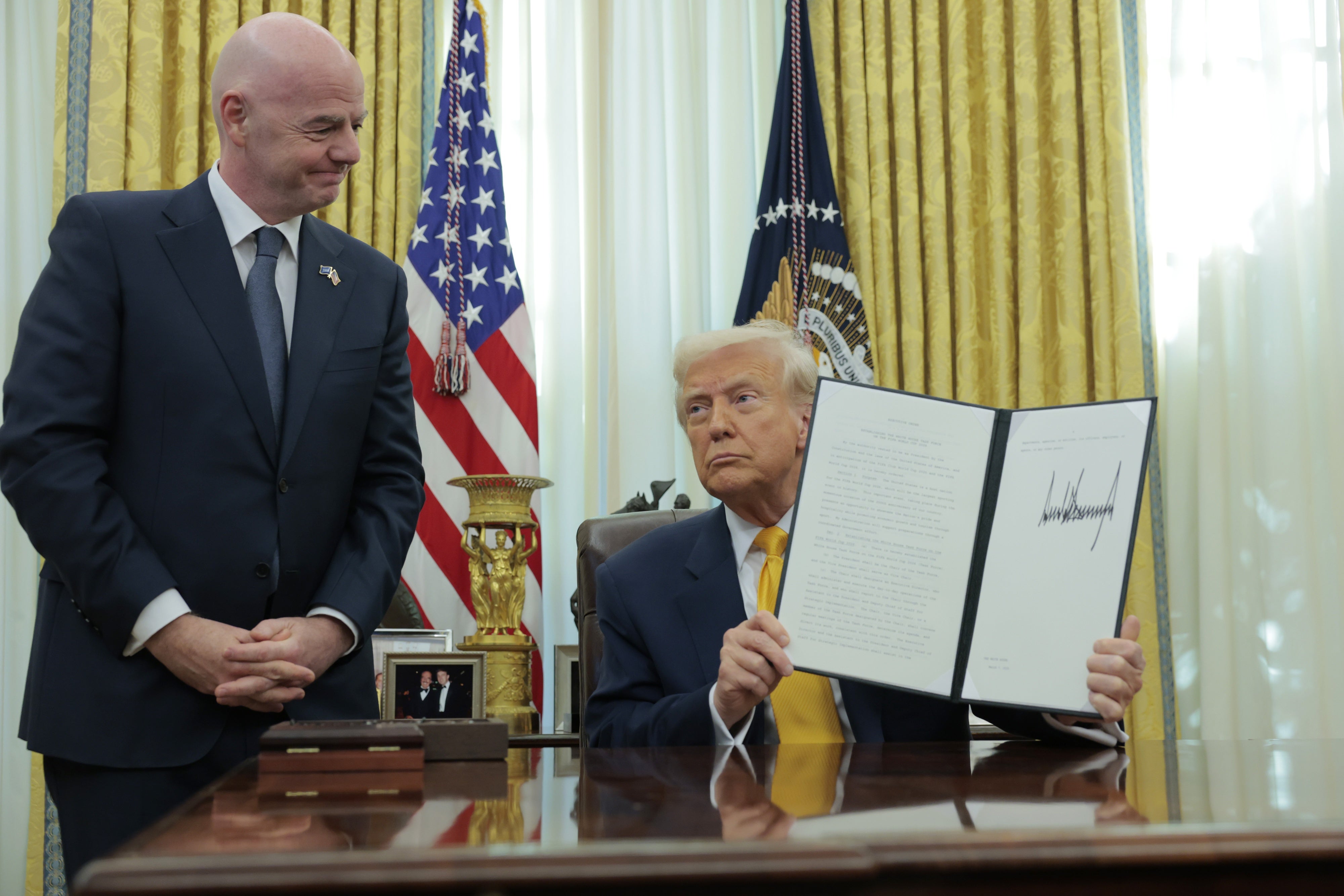 US President Donald Trump holds up an executive order alongside President of Fédération Internationale de Football Association (FIFA) Gianni Infantino in the Oval Office at the White House in Washington, DC,  March 7, 2025.