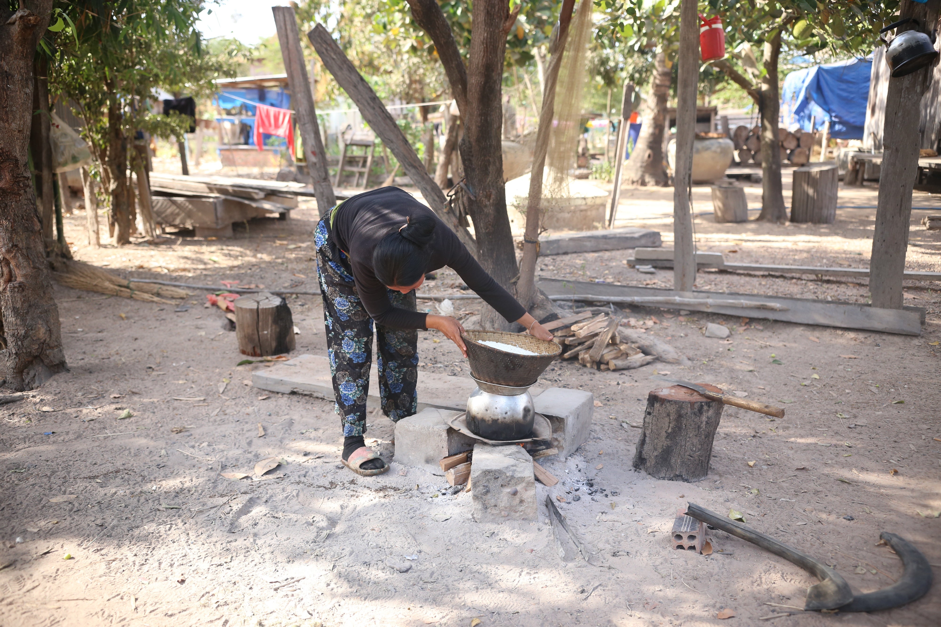 A woman stands over a pot on a fire outside