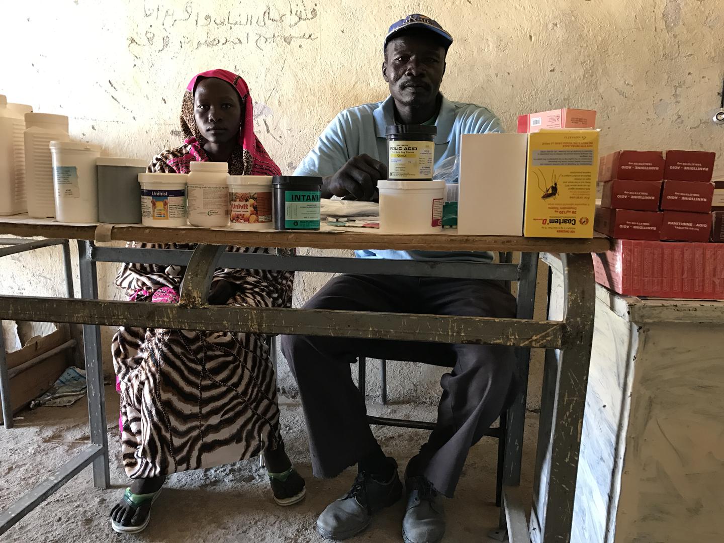 Mukuma Hamad, a volunteer health worker (L), and James Atai, a nurse, sit at a table displaying almost the total stock of basic medicines in the only health clinic in Hadara village, rebel-controlled Southern Kordofan. 