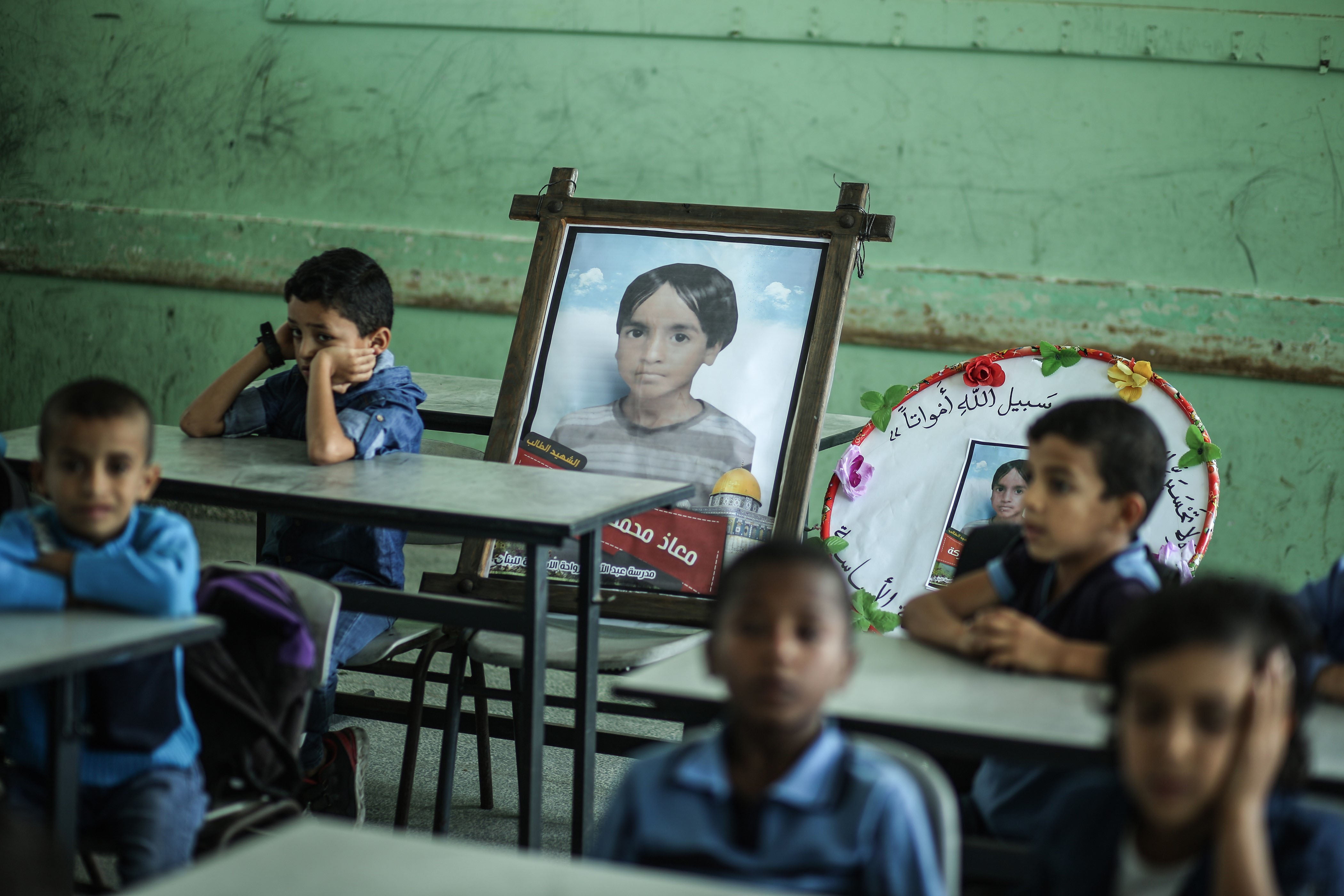 Children in Gaza sit on November 16, 2019 in a classroom near a picture of their classmate Mo’ath al-Sawarka, aged 7, one of five children killed in an Israeli airstrike two days earlier.
