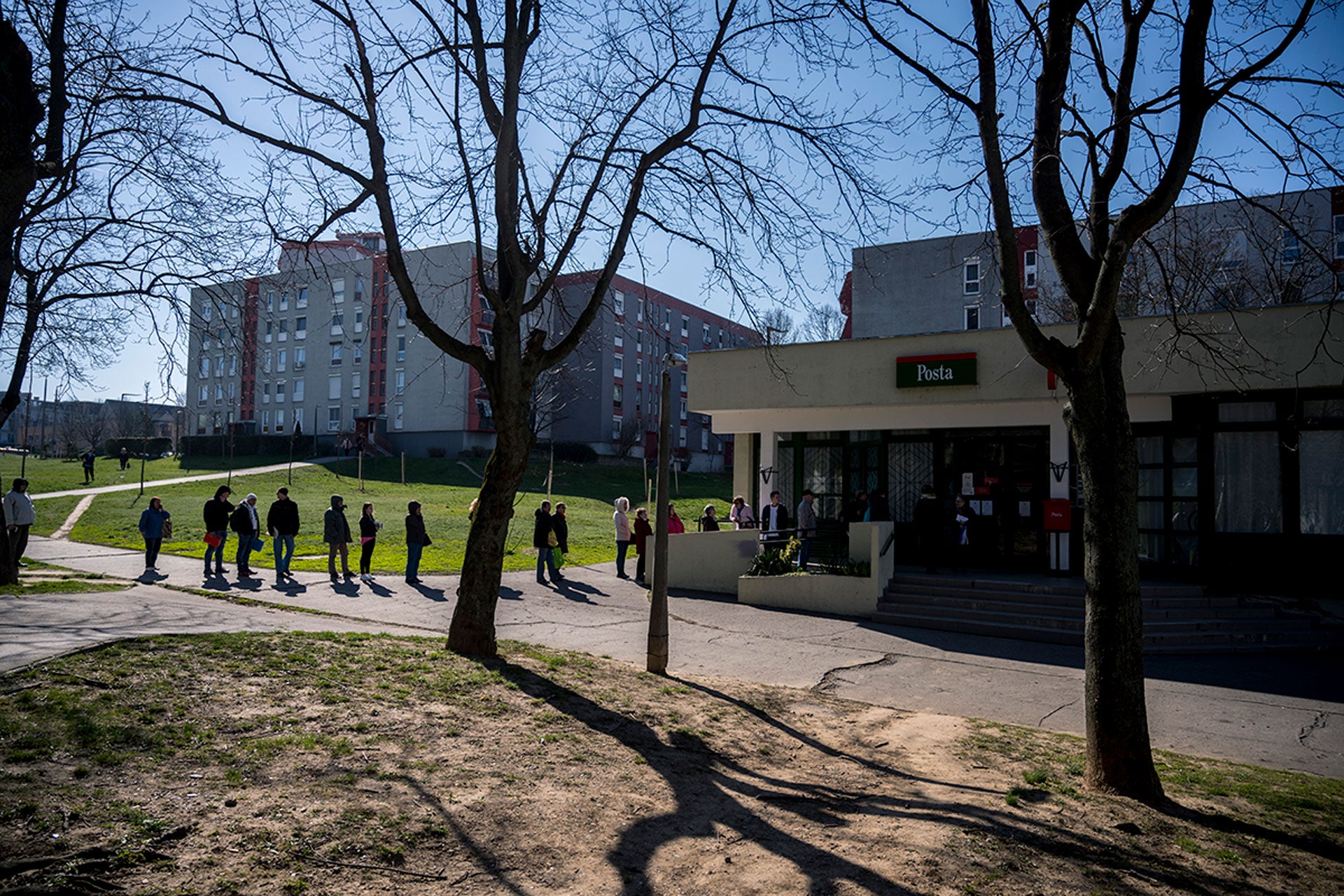 People keep their distance as they queue up in front of a post office in Pecs, Hungary, Monday, March 16, 2020.