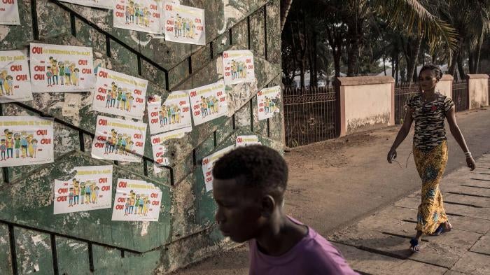Two people walk down a street in front of a wall covered in political posters