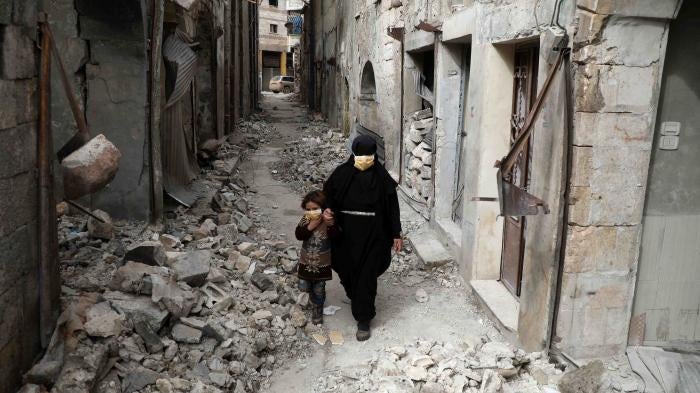 A woman in a black niqab and face mask walks through a deserted street with a child