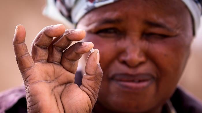 A woman squints while holding a small diamond in her fingers