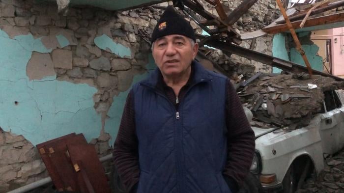 Interviewee stands in front of a ruined building