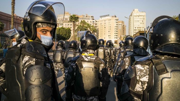 A group of uniformed police with riot gear stand on the street