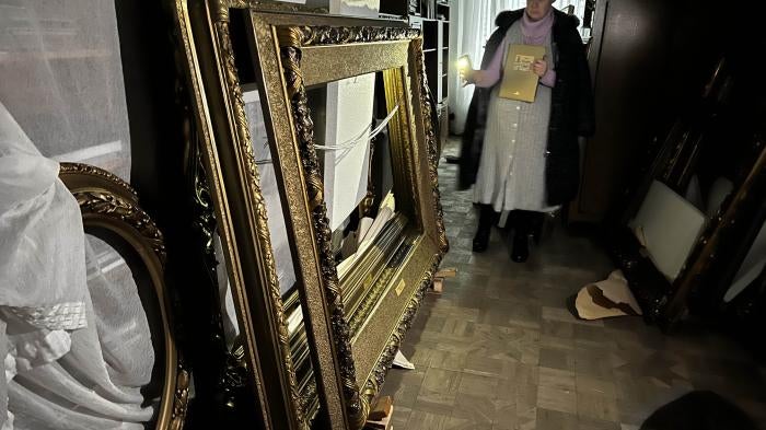 A woman shines a flashlight on a stack of empty picture frames