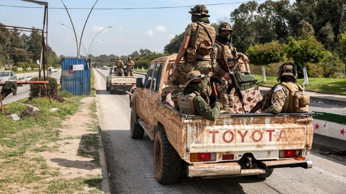 Uniformed and armed soldiers ride in the back of a truck