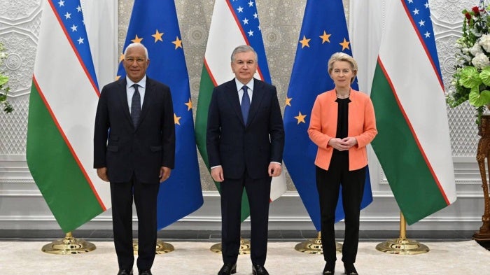 2 men and 1 woman pose for a photo in front of EU and Uzbekistan flags