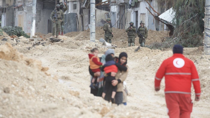 Women carry children as Israeli forces forcibly displace them from Nur Shams refugee camp 