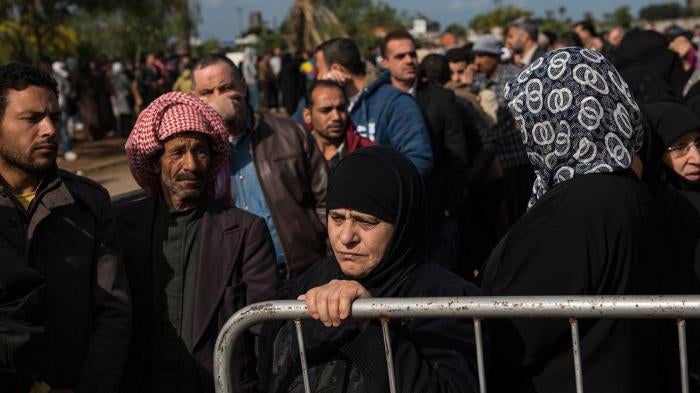 In Tripoli, Lebanon. Syrian Refugees line up to register or renew their registration at the UNHCR compound. A woman stands by a barrier. 