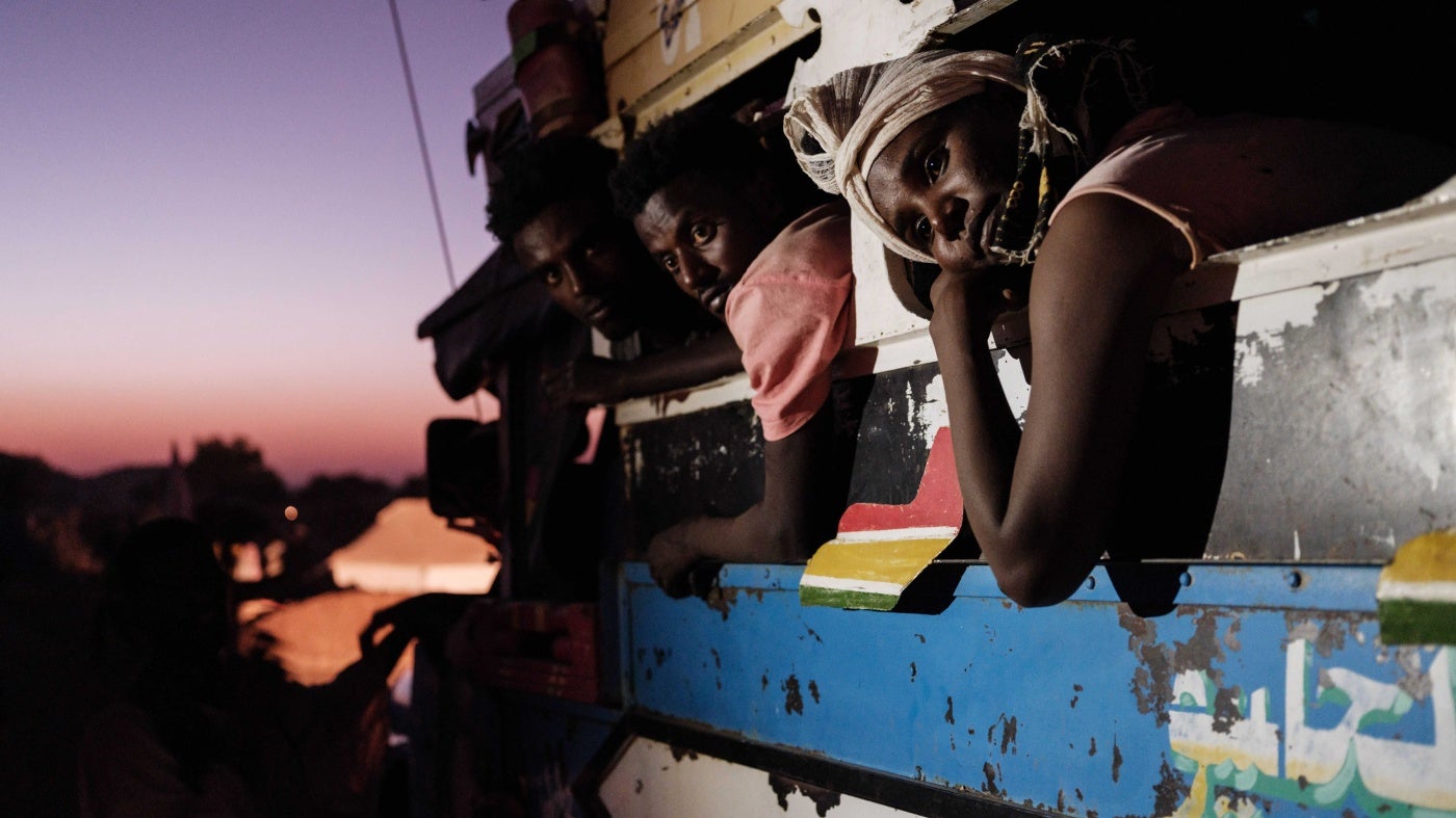Men and women lean out of the windows of a bus