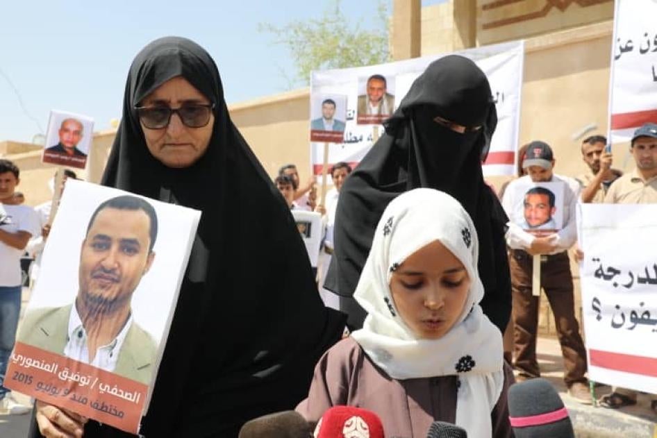 Tawfiq al-Mansouri's mother, daughter, and wife hold up a photo of him during a demonstration. Al-Mansouri is one of four imprisoned Yemeni journalists currently facing the death penalty.