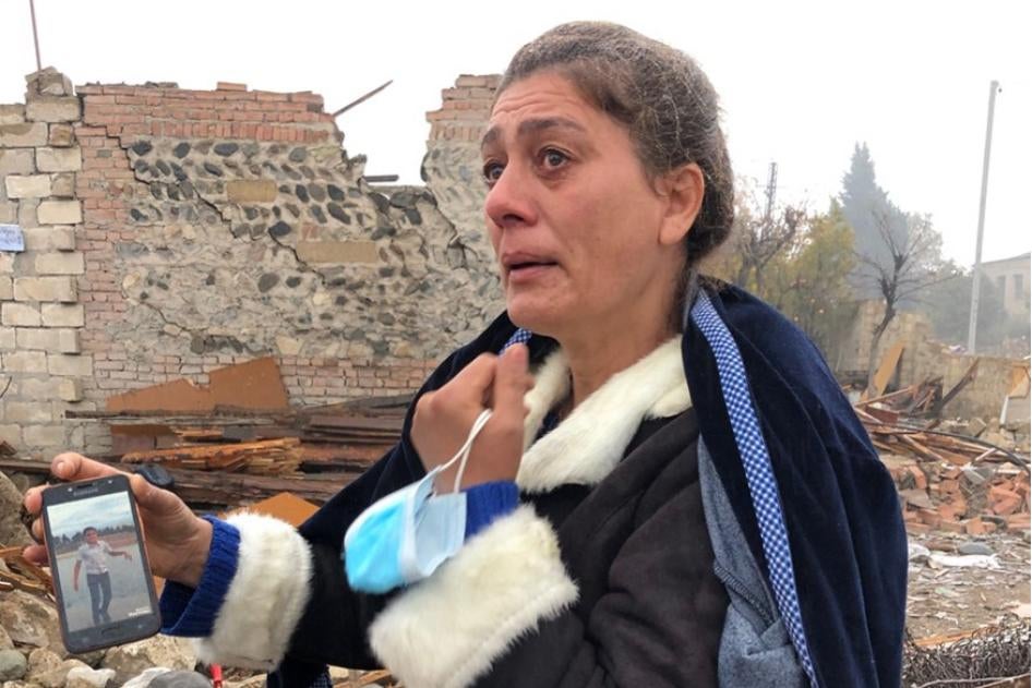 Shaira Guliyeva, 47, stands in front of her destroyed home and shows a photograph of her nephew, Arthur Guliyev, 13, who was killed there by a ballistic missile attack on October 17.