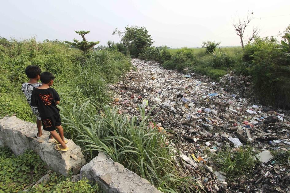 Two children stand above a river filled with garbage 