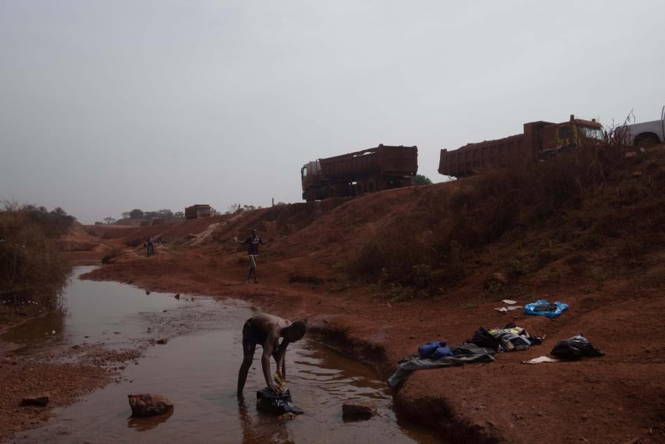 Un homme lave ses vêtements au bord d’une route utilisée par un consortium minier actif dans l’exploitation de la bauxite en Guinée. Les membres de communautés locales ont déclaré que la construction des routes minières a obstrué des rivières et ruisseaux, détournant leur cours et asséchant les puits locaux. 