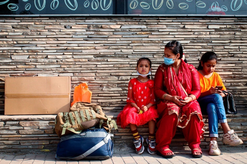 A woman and two young girls sit at a bus station