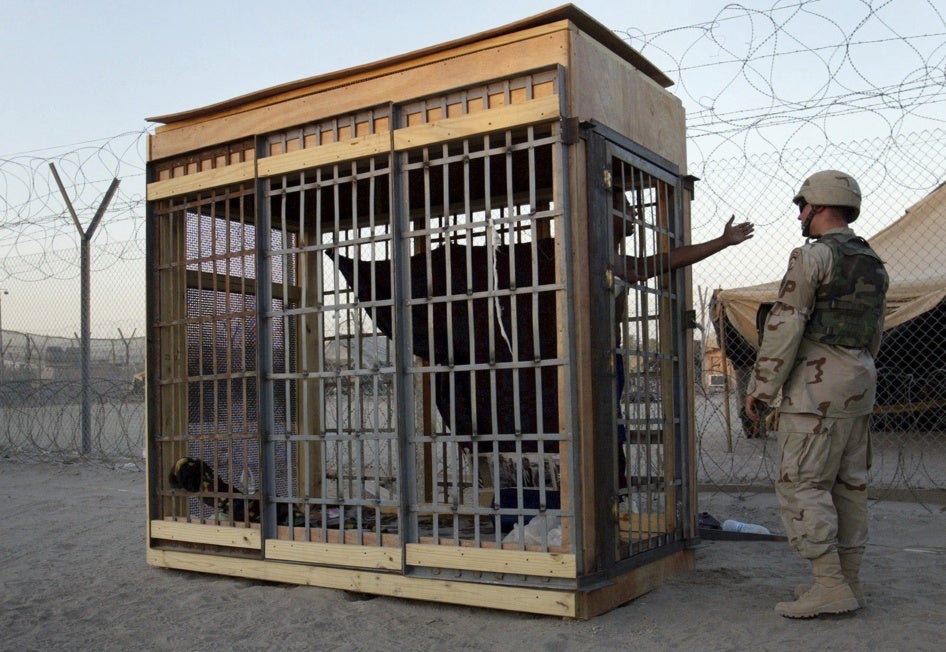 A detainee in an outdoor solitary confinement cell talks with a military police officer at the Abu Ghraib prison on the outskirts of Baghdad, Iraq, June 22, 2004. 