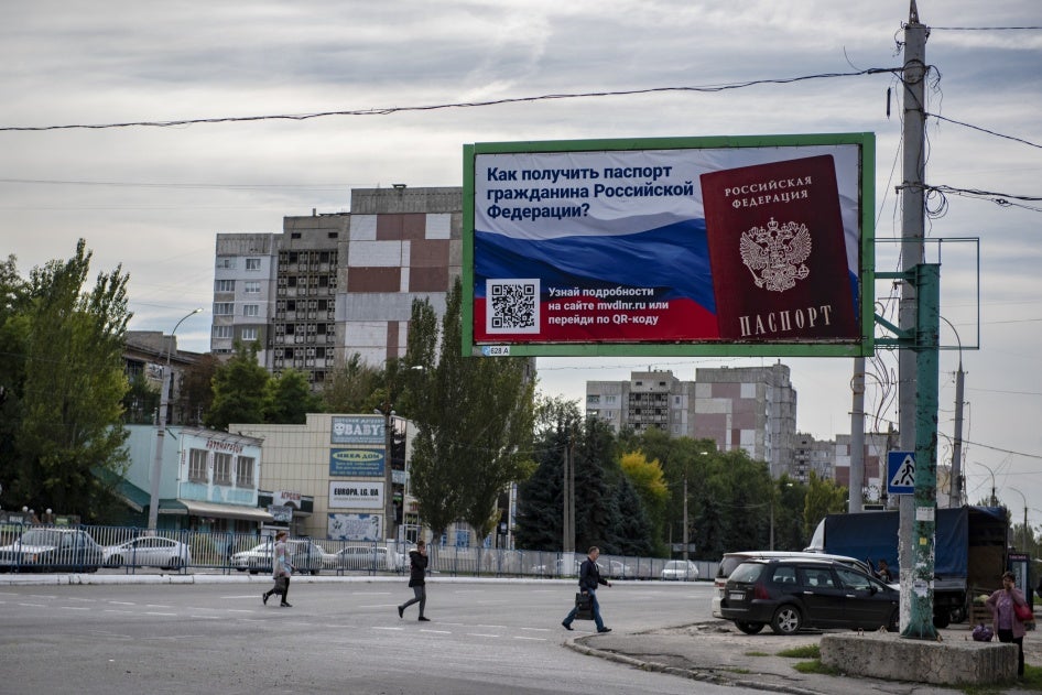 Menschen überqueren eine Straße mit einer Plakatwand, auf der zu lesen ist: „Wie man einen Pass als Bürger Russlands erhält“, im besetzten Gebiet von Luhansk, 22. September 2022.