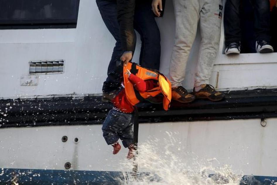 A toddler is saved from the Aegean Sea as one refugee hands the child to a volunteer lifeguard near the Greek island of Lesbos, October 30, 2015.