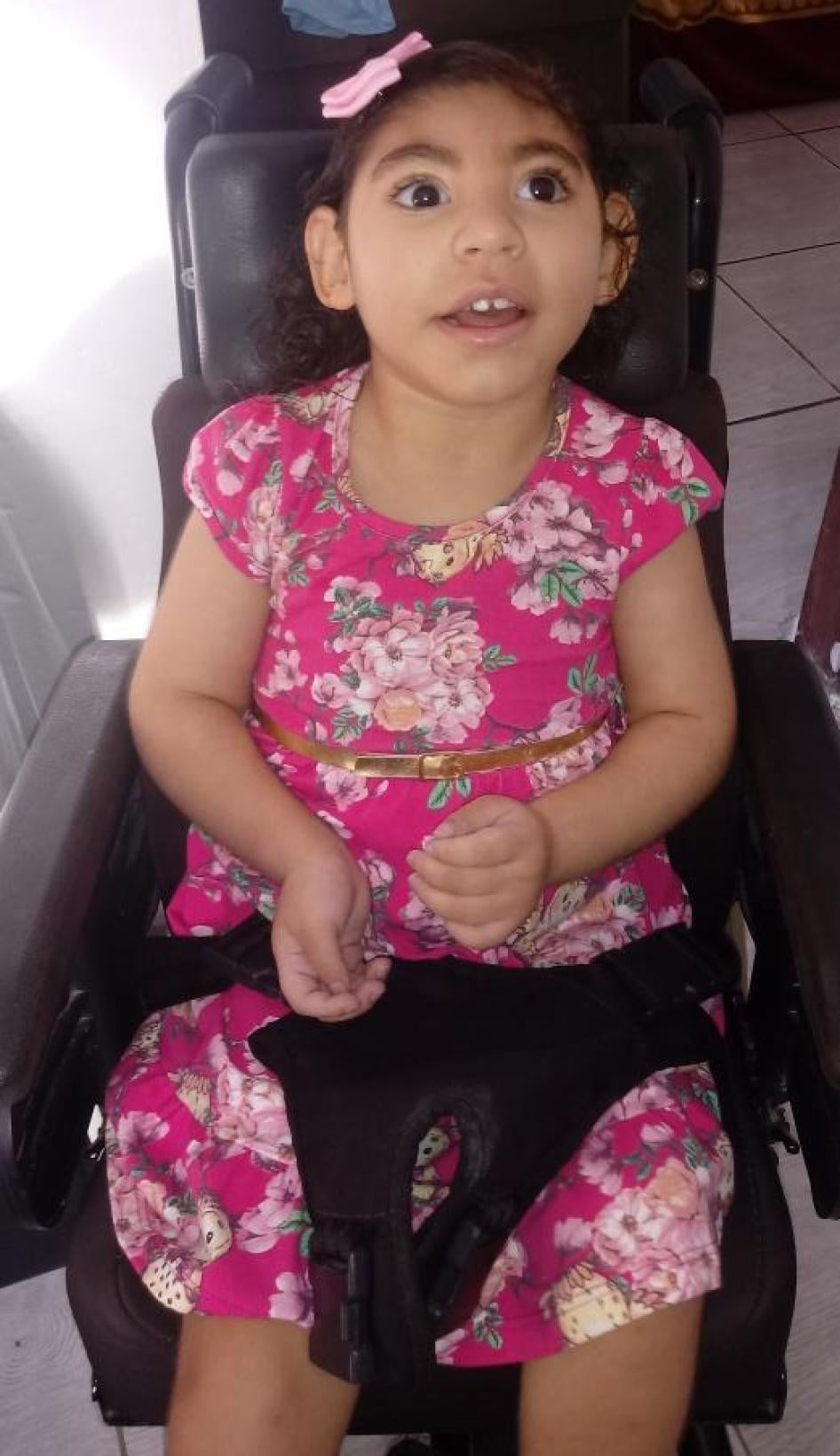 Com três anos, Gaby tem cabelos longos encaracolados, dois irmãos, e uma cadeira de rodas que a ajuda a se locomover pela casa.