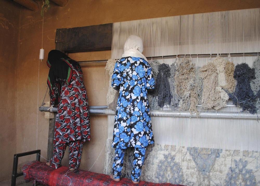 Marina, 15, left, and her sister, who is also under 18, work on a carpet loom at home in central Bamiyan province. Marina and her 10 siblings earn the family’s income through carpet weaving.
