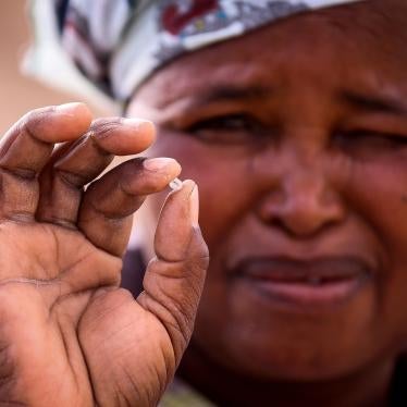 A woman squints while holding a small diamond in her fingers