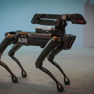 A black robot with four legs resembling a dog stands on a stage in front of a shite background.