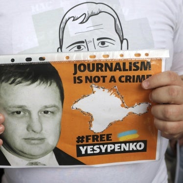 A man holds a placard that says "Journalism is Not a Crime" and "#FreeYesypenko"