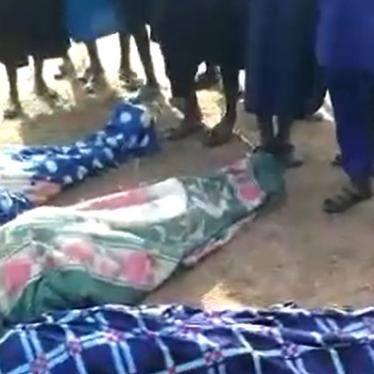 People stand over three bodies wrapped in fabric