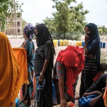 People collect water from a tank in a compound of abandoned buildings