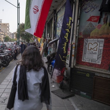 A young Iranian woman, who does not wear a mandatory headscarf, walks under an Iranian flag in downtown Tehran, Iran, September 29, 2024. 