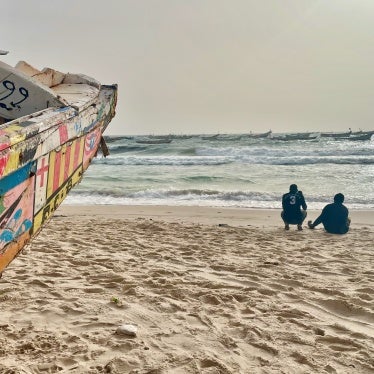Two men sitting on a beach near wooden boats
