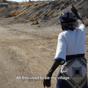 A picture of a woman pointing and saying. "All this used to be my village."