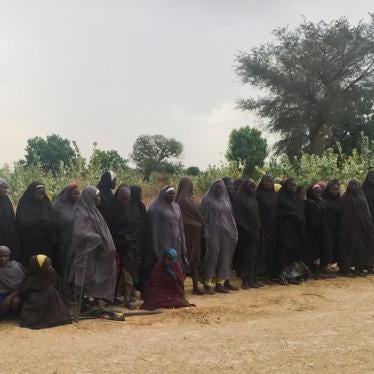 A man carrying a Boko Haram flag walks past a group of 82 Chibok girls, who were held captive for three years by Islamist militants, as the girls wait to be released in exchange for several militant commanders, near Kumshe, Nigeria May 6, 2017.