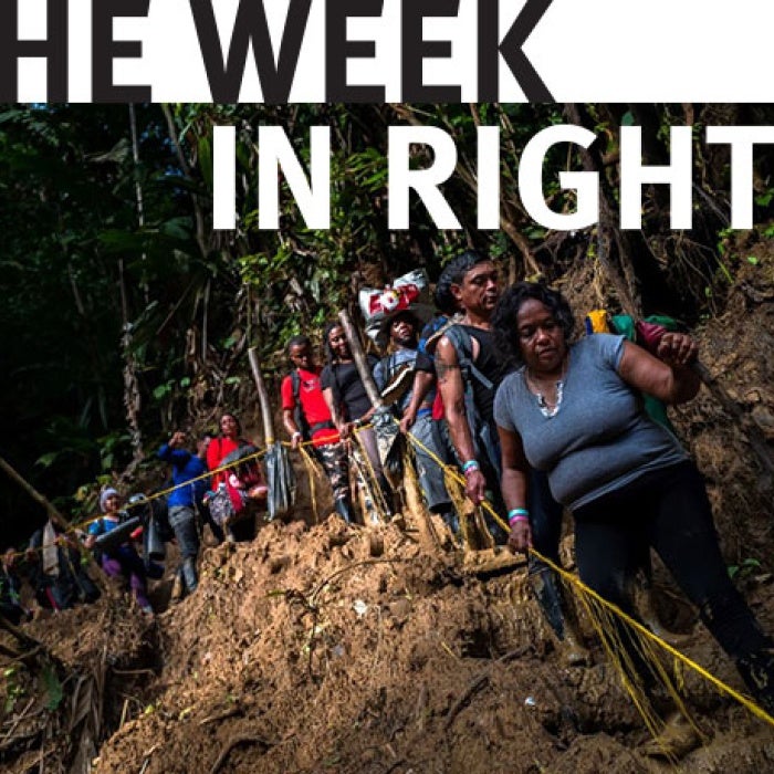 Migrants walk on trail along steep cliff. 